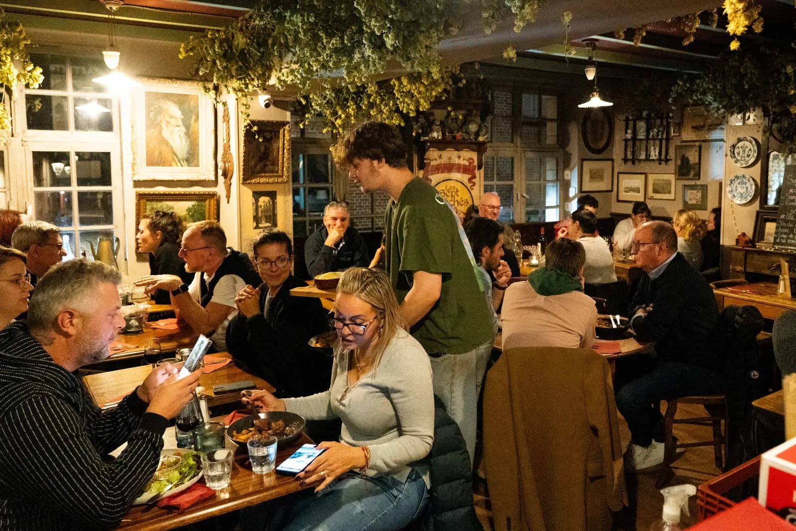 La salle aux cadres et aux assiettes de faïence, un serveur entre les tables.