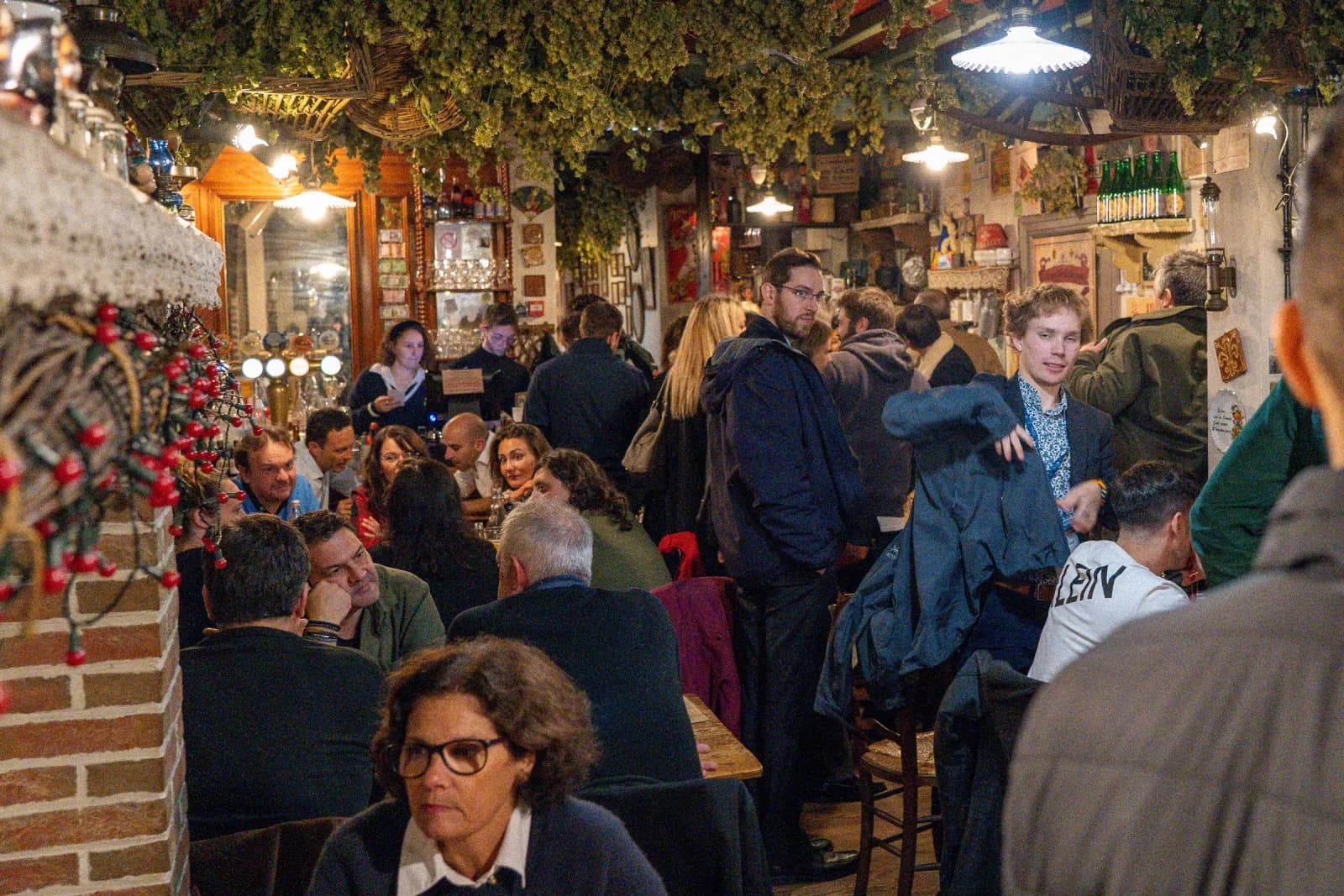 La salle pleine sous le houblon séché, le comptoir au fond.